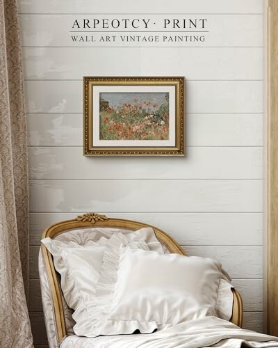 Vintage painting of a floral field in a frame on a wall above an elegant chair with cushions.